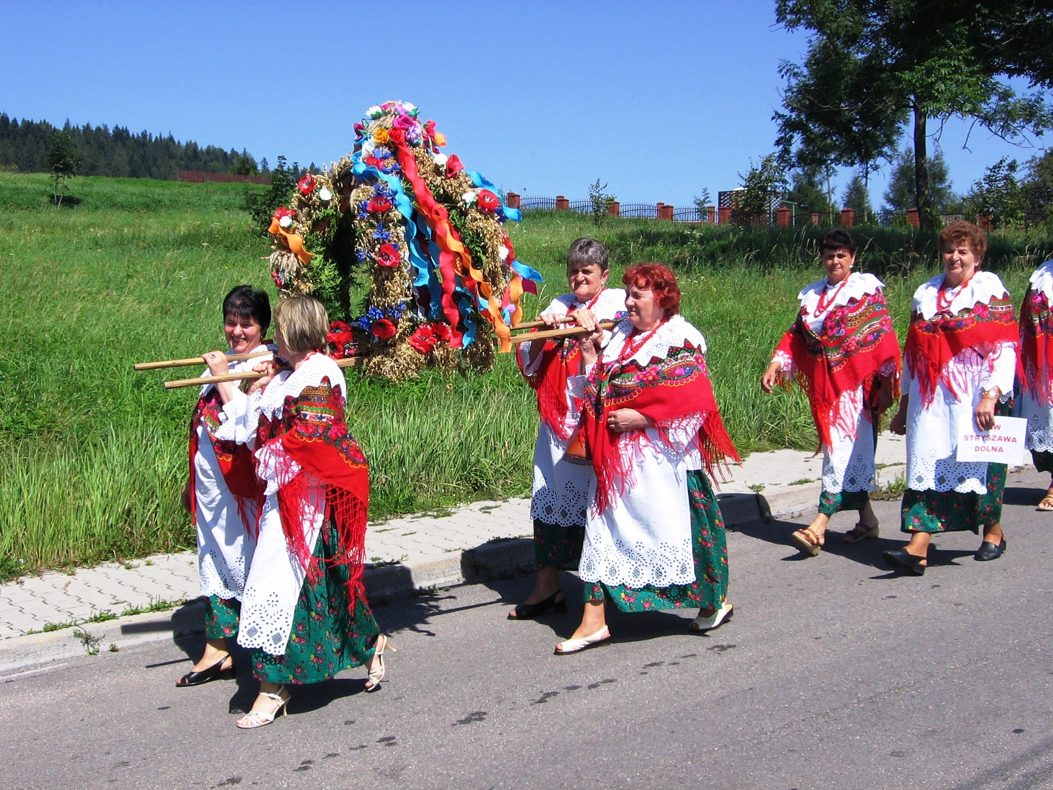 cztery kobiety w strojach ludowych niosą wieniec na lektyce